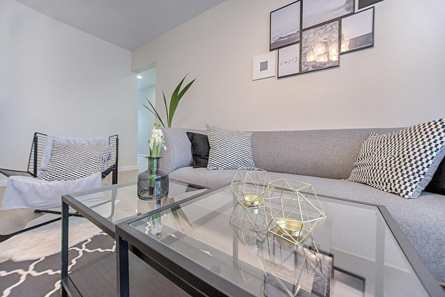 Gray-toned living room with a glass coffee table and a patterned rug.