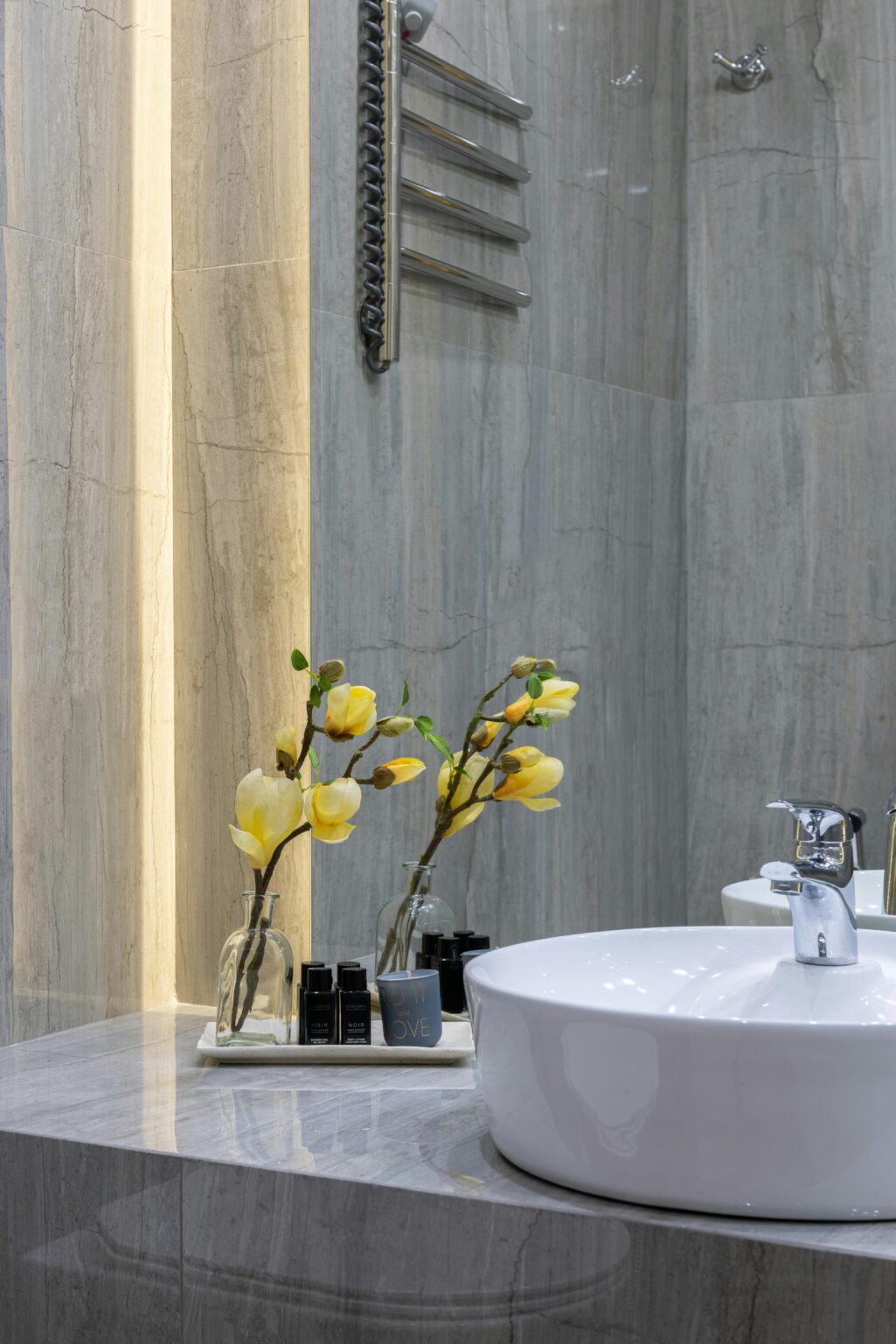 Spotless bathroom sink on a vanity with a vase holding yellow flowers next to it