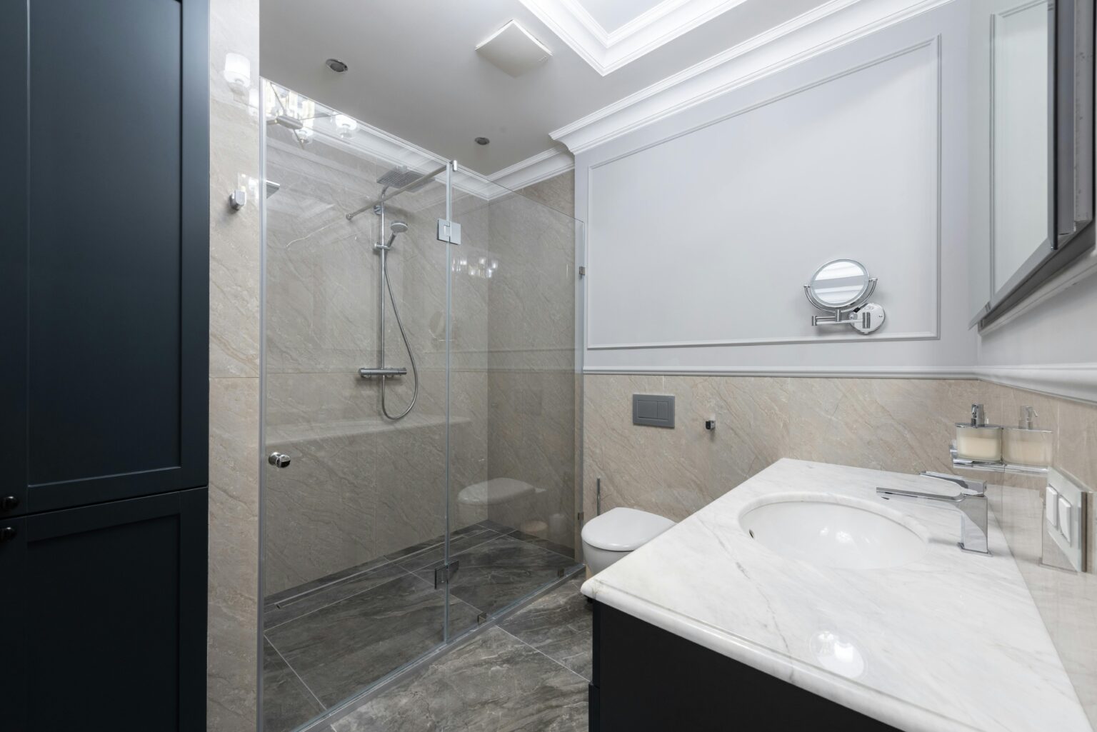 Modern bathroom featuring a glass-enclosed shower with rain-style showerhead, wall-mounted toilet, and marble countertop vanity against light beige and gray tile walls. Move-in move-out cleaning in Seabrook.